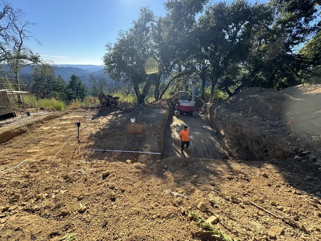 Graded lot with an excavator and rolling hills beyond