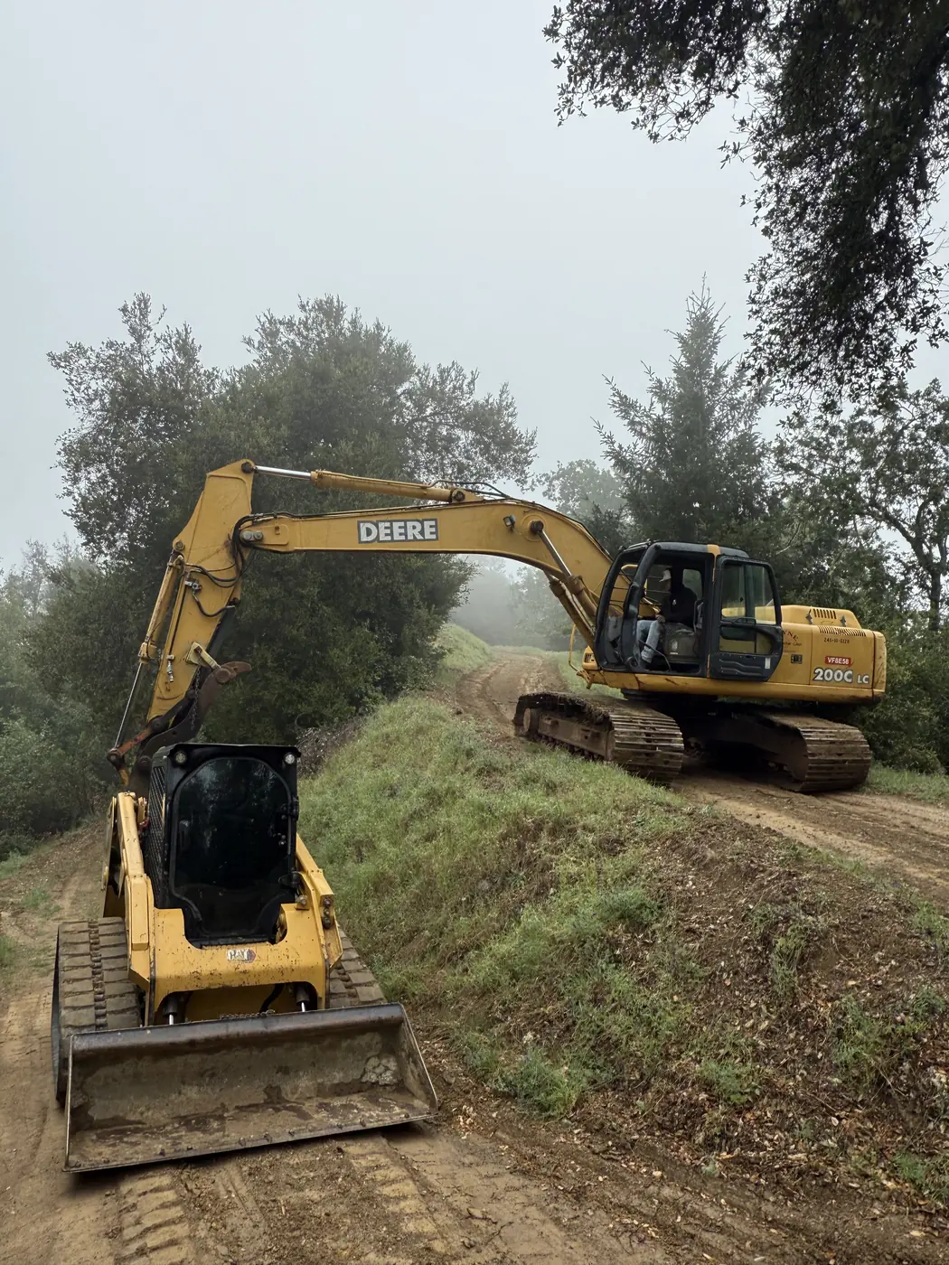 Excavator and skid steer clearing and cutting into a wooded hillside