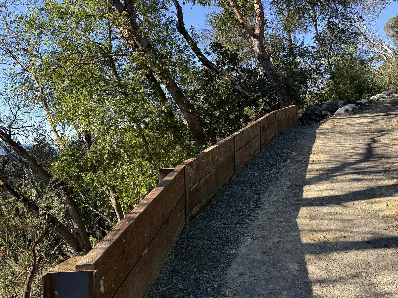 Completed wood lag retaining wall backfilled with drain rock along a hillside path