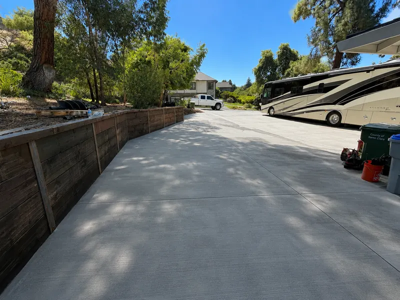 Finished wood retaining wall beside a broom finished concrete driveway with an RV parked alongside